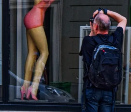 Monique · 09/05/2026 · 2781 x 5322 Cette photographie montre un homme prenant une photo d’une affiche publicitaire géante représentant une femme en maillot de bain coloré, posant de manière sensuelle. La composition oppose le sujet photographié (l’homme) et son reflet dans la vitrine.Le cadrage est serré sur les deux personnages, avec une lumière naturelle et diffuse. Les couleurs dominantes sont les tons chauds (rose, jaune) de l’affiche et les teintes neutres (bleu, gris) des vêtements de l’homme.L’ambiance est urbaine et légèrement ironique, mêlant quotidien et provocation visuelle. Le style est documentaire et spontané.