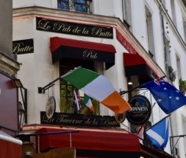 Deniz · 09/05/2026 · 6000 x 4000 Cette photographie montre la façade d’un restaurant parisien, "Le Pain de la Braise". Le sujet principal est l’enseigne et les trois drapeaux (irlandais, breton et français) accrochés à la rambarde.La composition est symétrique, avec un cadrage serré sur les éléments décoratifs. La lumière est naturelle, douce et légèrement tamisée, créant une ambiance chaleureuse. Les couleurs dominantes sont les tons rouges, blancs, verts et bleus, renforçant l’identité française et celtique.Le style est urbain et pittoresque, évoquant une ambiance typiquement parisienne et conviviale.