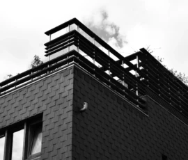 Deniz · 09/05/2026 · 5705 x 3973 Cette photographie met en scène un bâtiment avec un toit partiellement recouvert de végétation. Le sujet principal est la cheminée émettant de la fumée, suggérant une activité humaine.La composition est verticale, avec un cadrage serré sur la partie supérieure du bâtiment. La lumière, douce et diffuse, crée des contrastes marqués entre ombres et lumières, typiques d’un style photographique noir et blanc. Les tons dominants sont les gris et noirs, renforçant une ambiance à la fois industrielle et mélancolique. L’image évoque une atmosphère sobre et contemplative, mêlant nature et architecture.