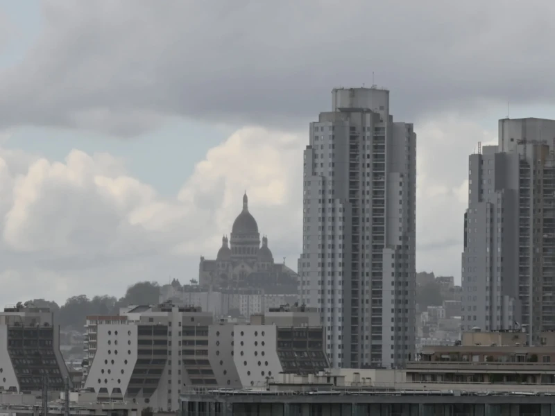 Pierre · 03/05/2026 · 2523 x 1678 Cette photographie montre une ville avec des gratte-ciels modernes en premier plan. Le sujet principal est un ensemble architectural contrasté : des bâtiments contemporains et une cathédrale historique en arrière-plan, partiellement visible.La composition est équilibrée, avec un cadrage large capturant une partie du ciel nuageux. La lumière est diffuse, atténuée par les nuages, créant une ambiance sobre. Les couleurs dominantes sont les tons gris et beiges, typiques d’un jour couvert. Le style est réaliste et documentaire, évoquant une atmosphère urbaine à la fois dynamique et mélancolique.