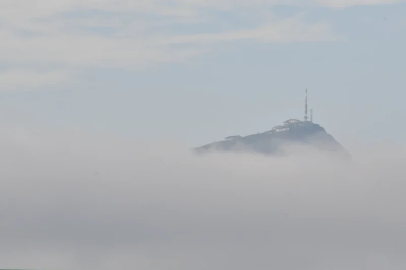 Vincent · 18/08/2023 · 3425 x 2284 Cette photographie met en scène un sommet montagneux émergent des nuages. Le sujet principal est une petite tour ou antenne située au sommet, à peine visible à travers la brume.La composition est épurée, centrée sur le contraste entre la montagne et le ciel nuageux. Le cadrage est large, capturant une vue immersive et atmosphérique. La lumière est douce et diffuse, adoucissant les contours.Les couleurs dominantes sont les teintes grises et bleutées, typiques d’un ciel brumeux. Le style est minimaliste et poétique, évoquant une ambiance mystérieuse et sereine, presque onirique.