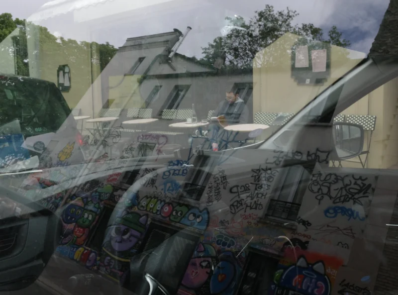 Bao · 5139 x 3809 Cette photographie montre principalement des graffitis colorés sur une surface vitrée ou métallique, reflétant aussi des bâtiments en arrière-plan. La composition joue sur les reflets et les motifs urbains, créant un effet de superposition entre réalité et image déformée.Le cadrage est serré, centré sur les tags et les éléments graphiques. La lumière semble naturelle mais diffuse, adoucissant les contrastes. Les couleurs dominantes sont vives et variées (bleus, roses, verts), typiques des graffitis. Le style est urbain et artistique, évoquant une ambiance dynamique et créative, presque onirique grâce aux déformations des reflets.