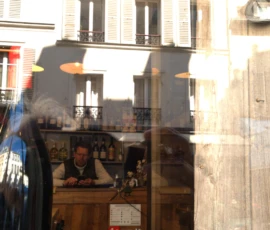 Bao · 6024 x 4016 Cette photographie montre une scène urbaine reflétée dans une vitre. Le sujet principal semble être un homme assis derrière un comptoir, probablement dans un café ou un bar. La composition joue sur les reflets et les ombres, créant une superposition entre intérieur et extérieur.Le cadrage est serré, capturant des détails flous et des éléments architecturaux. La lumière est naturelle, douce et légèrement dorée, suggérant un moment en fin de journée. Les couleurs dominantes sont des tons neutres (beiges, gris) avec des éclats de brun et de noir.L’ambiance est intimiste et légèrement mélancolique, évoquant une atmosphère calme et contemplative.