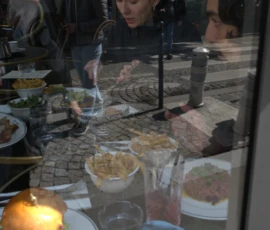 Bao · 6024 x 4016 Cette photographie montre un repas en intérieur, probablement dans un restaurant. Le sujet principal est une table garnie de plats variés : salades, viandes, et accompagnements. La composition est dynamique, avec des couverts et des assiettes disposés de manière informelle.Le cadrage est serré, mettant en valeur les détails des plats et les mains des convives. La lumière est douce et tamisée, créant une ambiance chaleureuse et intime. Les couleurs dominantes sont les tons chauds (beige, brun) et quelques touches de vert et rouge des aliments. Le style est réaliste et spontané, évoquant une ambiance conviviale et décontractée.