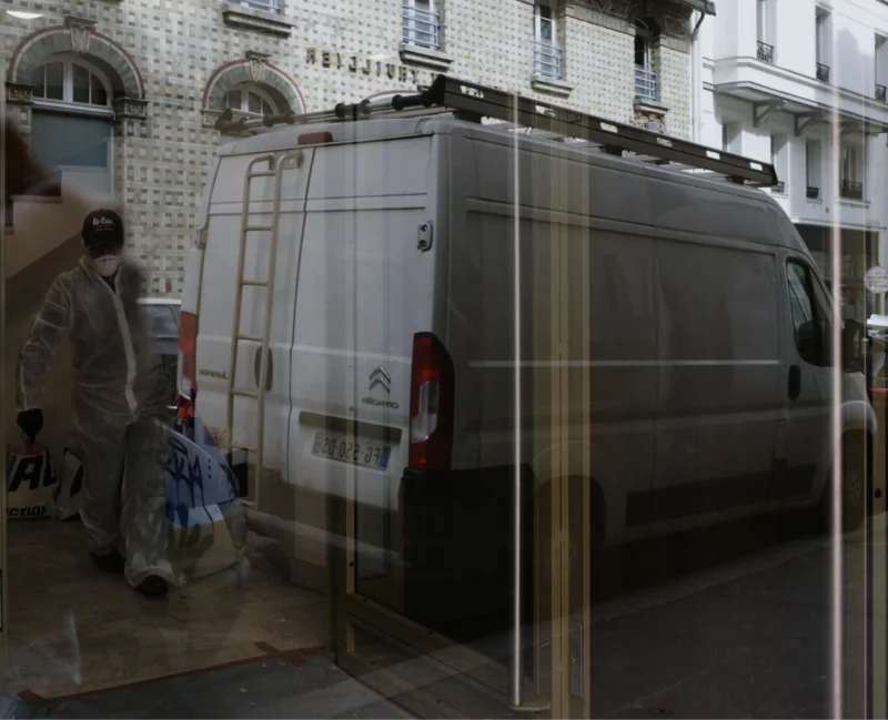 Bao · 4202 x 3408 Cette photographie montre un van utilitaire garé devant un bâtiment, partiellement reflété sur une surface vitrée.Le sujet principal est le véhicule, partiellement transparent et flouté. La composition inclut aussi une personne avec des sacs, partiellement visible. Le cadrage est serré, centré sur le van et son reflet.La lumière semble naturelle, mais diffuse, créant des contrastes doux. Les couleurs dominantes sont les tons gris et beiges, avec des touches de bleu et de noir.Le style est réaliste et urbain, avec une ambiance un peu floue et mystérieuse due aux reflets et au flou.