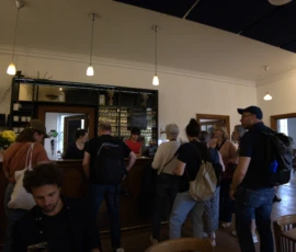 Bao · 5063 x 4016 Cette photographie montre un groupe de personnes dans un café ou un espace similaire. Le sujet principal est l'interaction sociale entre les individus, certains discutant ou attendant leur tour.La composition est dynamique, avec un cadrage serré sur les personnes en mouvement. La lumière est douce et naturelle, éclairant uniformément l’espace. Les couleurs dominantes sont neutres, avec des tons beiges, gris et quelques touches de rouge et vert. L’ambiance est conviviale et informelle, reflétant un lieu de rencontre et de détente. Le style est documentaire et spontané.
