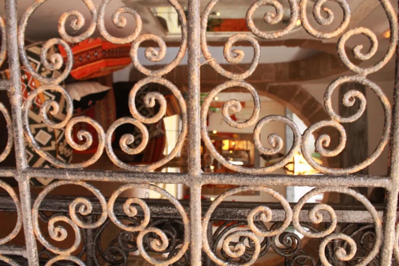 Sophie · 06/09/2025 · 4272 x 2848 Cette photographie montre une grille en fer forgé ornée de motifs décoratifs en spirales. Le sujet principal est cette grille, qui encadre partiellement une scène intérieure floue.La composition est symétrique, avec des motifs répétitifs. Le cadrage est serré, mettant en valeur les détails des spirales. La lumière est douce et naturelle, éclairant les motifs et créant des contrastes subtils.Les couleurs dominantes sont des tons neutres : gris, beige et brun. Le style évoque l'artisanat traditionnel et le charme vintage. L’ambiance est à la fois élégante et chaleureuse, avec une touche de nostalgie.
