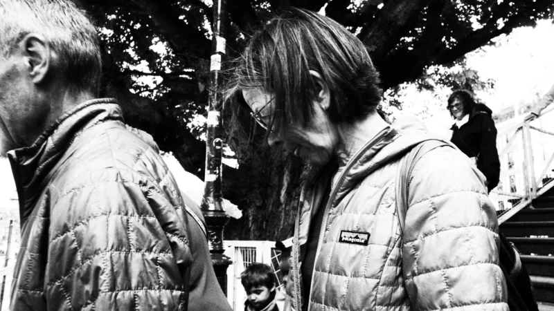 Dominique · 20/05/2026 · 6192 x 3480 Cette photographie en noir et blanc met en scène deux hommes comme sujets principaux. Le cadrage serré montre leurs visages en contre-plongée, créant une intimité. L’un semble observer l’autre à travers un appareil photo, suggérant une interaction réfléchie.La composition joue sur les reflets et les ombres, renforçant une ambiance contemplative. La lumière douce, probablement naturelle, adoucit les traits et ajoute une touche mélancolique. Le style, sobre et artistique, évoque un moment introspectif, presque cinématographique. Les couleurs dominantes, absentes en raison du noir et blanc, laissent place à des contrastes de tons clairs et sombres, accentuant l’émotion et la profondeur.
