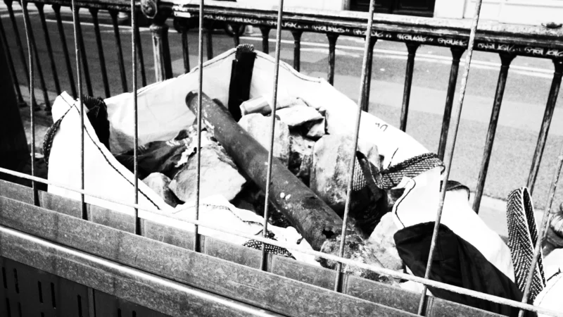 Dominique · 20/05/2026 · 6192 x 3480 Cette photographie en noir et blanc montre un sujet principal difficile à identifier clairement, probablement un animal mort, allongé sur le sol.La composition est simple, avec un cadrage serré derrière une barrière métallique. La lumière semble naturelle, mais contrastée, accentuant les ombres et les détails. Les couleurs dominantes sont les tons de gris, typiques du noir et blanc.Le style est documentaire et brut, évoquant une ambiance sombre et mélancolique, voire tragique. L'image suggère une scène de négligence ou d'abandon.