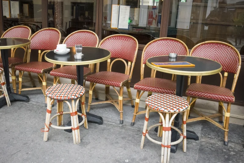 Dominique · 20/05/2026 · 2000 x 1333 Cette photographie montre une terrasse de café urbaine. Le sujet principal est composé de tables et chaises en métal avec des coussins rouges et motifs géométriques. La composition est symétrique, avec des tables rondes noires et des chaises disposées en rangées.Le cadrage est serré, centré sur les tables et chaises. La lumière semble naturelle, probablement en journée, avec des ombres douces. Les couleurs dominantes sont le rouge des coussins, le noir des tables, et le gris métallique des chaises. Le style est épuré et fonctionnel, évoquant une ambiance parisienne typique. L'atmosphère est calme et invitante, propice à une pause détente.