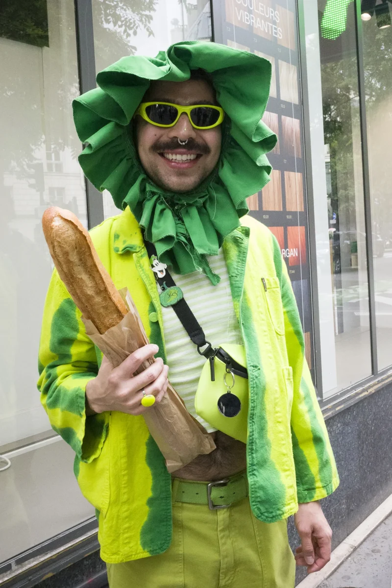 Dominique · 20/05/2026 · 1200 x 1800 Cette photographie montre un individu vêtu d’un costume humoristique représentant un personnage de "Jérôme Bonnet" (style fromage). Le sujet principal est au centre, portant un chapeau vert en forme de fromage, des lunettes et une tenue jaune-verte.Le cadrage est serré, mettant en valeur les détails du déguisement. La lumière est naturelle et semble provenir d’une source frontale, éclairant bien le sujet. Les couleurs dominantes sont le jaune fluo et le vert, créant un contraste vif. L’ambiance est festive et décalée, évoquant une ambiance de carnaval ou de fête déguisée.
