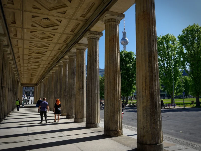 Cyrille · 01/05/2026 · 2026 x 1520 Cette photographie montre une colonnade classique avec des colonnes imposantes. Le sujet principal est l’architecture, mettant en valeur une perspective profonde.La composition repose sur des lignes droites et symétriques, guidant le regard vers l’horizon. Le cadrage est serré sur les colonnes, avec une ouverture vers un parc et un monument distant.La lumière est naturelle et vive, créant des contrastes nets. Les couleurs dominantes sont les tons gris-beige des colonnes, rehaussés par le vert des arbres et le bleu du ciel.Le style est architectural et classique, évoquant une ambiance à la fois historique et sereine.