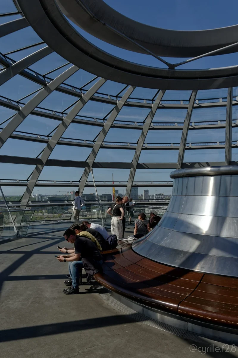 Cyrille · 01/05/2026 · 1347 x 2026 Cette photographie montre un groupe de personnes dans une structure architecturale moderne, probablement un dôme de verre. Le sujet principal semble être l’observation depuis une plateforme circulaire en bois, avec une vue vers le bas à travers une ouverture centrale.La composition met en valeur les lignes géométriques du dôme et la perspective verticale. Le cadrage est serré, centré sur les visiteurs et l’ouverture. La lumière est naturelle, traversant le verre et créant des contrastes lumineux. Les couleurs dominantes sont les tons froids du verre et du métal, avec des touches chaudes du bois.L’ambiance est à la fois futuriste et contemplative, évoquant une expérience immersive et technologique.