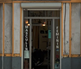 Cyrille · 16/05/2026 · 900 x 1200 Cette photographie montre la façade d’un salon de coiffure nommé "Bicoudi Coiffure". Le sujet principal est l’entrée du magasin, avec ses vitrines et enseignes.La composition est symétrique, avec des colonnes encadrant l’entrée. Le cadrage est serré, mettant en valeur les détails architecturaux et les inscriptions.La lumière est tamisée, créant une ambiance chaleureuse et légèrement nostalgique. Les couleurs dominantes sont les tons jaunes, blancs et bleus, renforçant un style rétro et artisanal. L’ambiance évoque un lieu typique et authentique, peut-être un peu vieillissant mais plein de caractère.