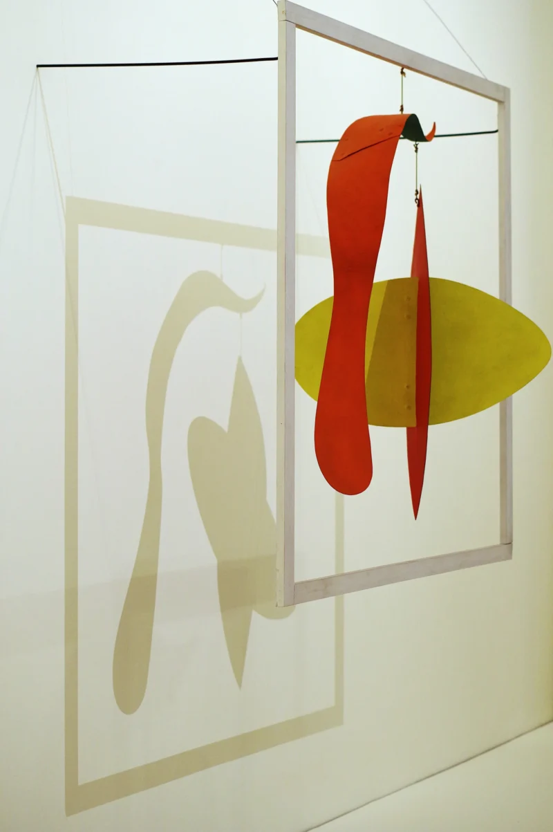 Agnes · 23/05/2026 · 4000 x 6016 Cette photographie présente une œuvre artistique moderne composée de deux éléments suspendus. Le sujet principal est une silhouette blanche stylisée, évoquant une forme humaine ou animale, et un objet coloré en forme de goutte jaune et rouge suspendu devant.La composition est épurée, avec un cadrage serré sur les formes géométriques. La lumière est douce et uniforme, mettant en valeur les contours nets. Les couleurs dominantes sont le blanc, le jaune et le rouge, créant un contraste saisissant. Le style est abstrait et minimaliste, évoquant une ambiance à la fois artistique et épurée, presque méditative.