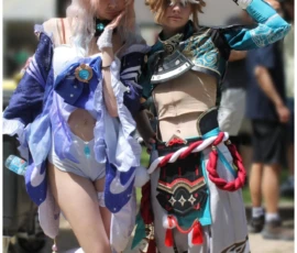 Sophie · 24/05/2026 · 1428 x 2283 Cette photographie met en scène deux personnes vêtues de costumes cosplay colorés. Le sujet principal semble être un duo en pleine interaction, l’un déguisé en personnage féminin élégant et l’autre en personnage masculin excentrique.La composition est dynamique, avec un cadrage serré sur les deux personnages. La lumière est naturelle et semble provenir d’une source externe, créant des contrastes doux. Les couleurs dominantes sont vives : bleu, violet, rose et turquoise.Le style est festif et ludique, évoquant une ambiance de convention ou de festival déguisé. L’énergie et la joie transparaissent, renforçant une ambiance joyeuse et créative.