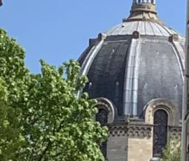 Kerry · 09/05/2026 · 1754 x 3800 Cette photographie met en scène une partie d’un édifice religieux, probablement une cathédrale ou une église, avec une coupole et une flèche surmontée d’une croix. Le cadrage est serré sur ces éléments architecturaux, encadrés par des feuilles vertes en bas.La lumière est naturelle et semble ensoleillée, créant des contrastes nets. Les couleurs dominantes sont les tons gris-beige de la pierre, le vert des feuilles et le bleu du ciel. Le style est photographique classique, réaliste, mettant en valeur l’élégance et la grandeur de l’architecture. L’ambiance est sereine et majestueuse.