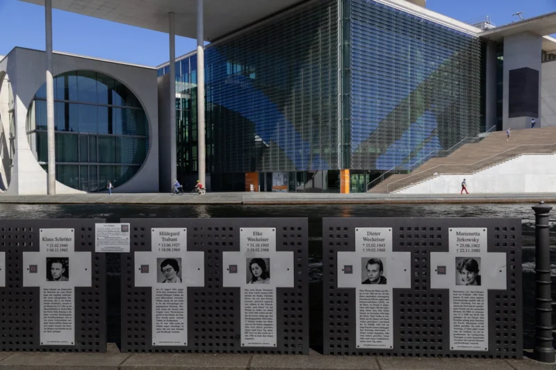 Muriel · 01/05/2026 · 2048 x 1365 Cette photographie montre une série de plaques commémoratives en mémoire des victimes, probablement des attentats du 11 septembre ou d'un autre événement tragique. Le sujet principal est ces plaques disposées en rangée devant un bâtiment moderne.La composition est symétrique et ordonnée, avec un cadrage serré sur les plaques. La lumière est naturelle et semble provenir d’un angle élevé, éclairant uniformément la scène. Les couleurs dominantes sont neutres, avec des tons gris et blancs, renforçant une ambiance sobre et respectueuse. Le style est épuré et commémoratif, évoquant gravité et recueillement.