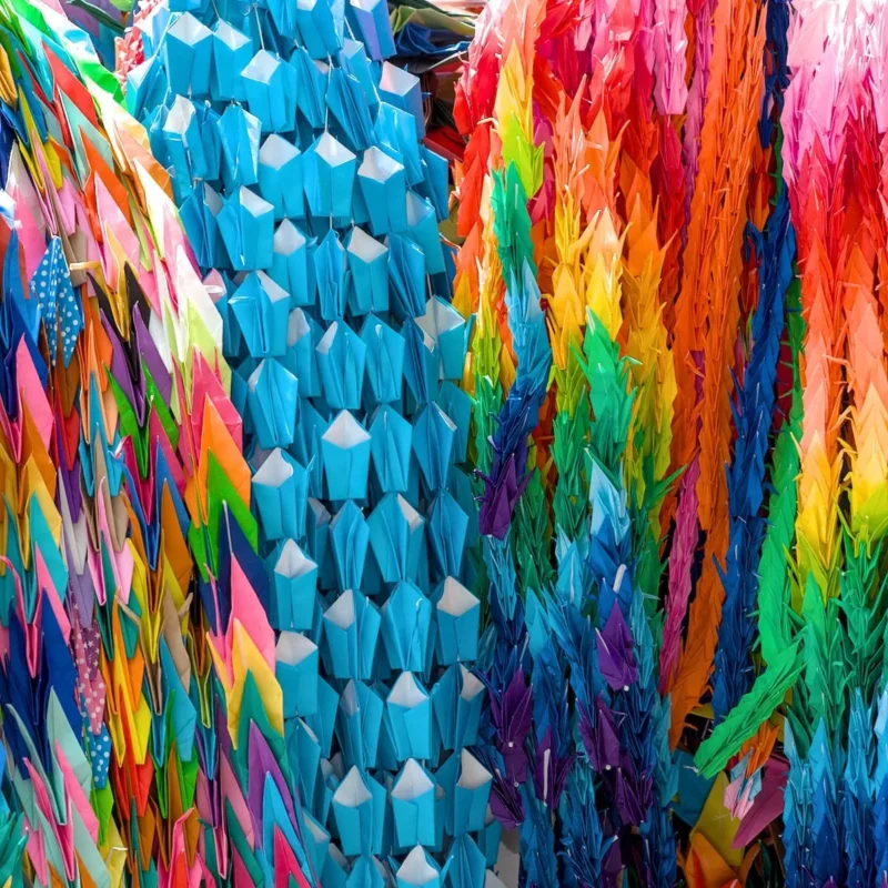 Thibault · 29/05/2017 · 1200 x 1200 Cette photographie met en scène une structure textile colorée, probablement une installation artistique ou un objet décoratif. Le sujet principal est une série de triangles bleus disposés en motif géométrique, entourés de franges multicolores.Le cadrage est serré, mettant en valeur les détails des textures et des couleurs. Les couleurs dominantes sont le bleu, le rouge, le vert et le jaune, créant un effet vibrant et dynamique. La lumière semble naturelle, éclairant uniformément la scène.L’ambiance est festive et joyeuse, évoquant un style artistique moderne et créatif, presque psychédélique.