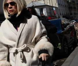 Muriel · 16/05/2026 · 1365 x 2048 Cette photographie met en scène une femme comme sujet principal, vêtue d’un long manteau en fourrure blanche et d’une mini-jupe, avec un accessoire à la main. Le cadrage est serré, centré sur elle, avec un arrière-plan flou montrant des bâtiments et des objets urbains.La lumière est naturelle et vive, créant des contrastes marqués. Les couleurs dominantes sont les tons blancs et gris, adoucis par des touches de noir et de bleu. Le style est urbain et élégant, évoquant une ambiance chic et moderne, malgré un côté décontracté. L’atmosphère suggère une ville animée, avec une touche de sophistication.