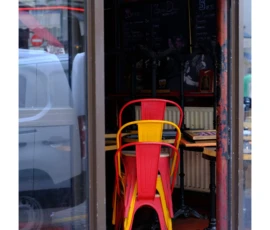 Julia · 09/05/2026 · 1583 x 2814 Cette photographie montre un **siège de bar rouge et jaune** comme sujet principal, placé devant une entrée vitrée. La composition est simple, avec un cadrage serré sur le siège et une partie de l’espace intérieur flou en arrière-plan.La lumière semble naturelle, avec des ombres douces et une teinte légèrement chaude. Les **couleurs dominantes** sont le rouge vif, le jaune et des tons neutres (gris, beige). Le style est réaliste et urbain, évoquant une ambiance **moderne et un peu désordonnée**, typique d’un local commercial ou d’un café.