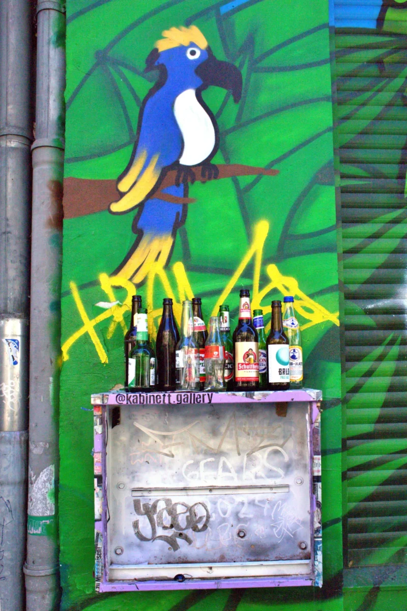 Fabienne · 02/05/2026 · 3192 x 4788 Cette photographie montre une fresque murale colorée intégrant un **sujet principal** : un **oiseau exotique** stylisé, aux couleurs vives (bleu, jaune). En dessous, une **boîte électrique** est transformée en bec d'oiseau, avec des fils et des ampoules évoquant des dents.La **composition** est dynamique, avec un **cadrage serré** mettant en valeur les détails. Les **couleurs dominantes** sont le **vert**, le **bleu** et le **jaune**, créant un contraste joyeux. Le **style** est **urbain et artistique**, mêlant street art et récupération d'éléments techniques.L’**ambiance** est **fantaisiste et créative**, avec une touche de **surrealisme**. La lumière semble naturelle, mettant en valeur les teintes vives.