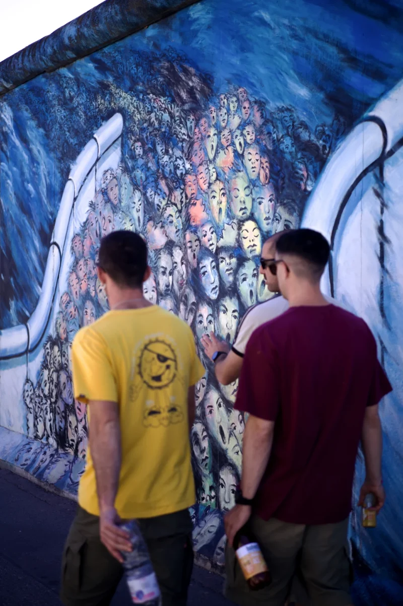 Thomas · 02/05/2026 · 1362 x 2048 Cette photographie montre deux hommes observant un mural coloré. Le sujet principal est le graffiti derrière eux, représentant des visages stylisés et des motifs oniriques.La composition est dynamique, avec un cadrage serré sur les personnages et l’œuvre. La lumière semble naturelle, bien répartie, éclairant les sujets sans ombres marquées. Les couleurs dominantes sont vives et contrastées : bleus profonds, jaunes, rouges et blancs.Le style est artistique et urbain, évoquant une ambiance créative et festive. L'atmosphère est à la fois contemplative et énergique, reflétant l’engouement pour l’art de rue.