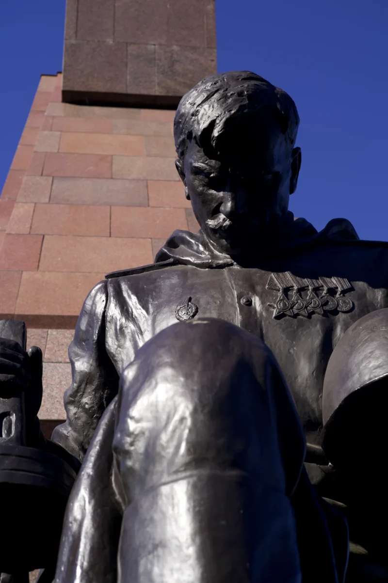 Thomas · 02/05/2026 · 1362 x 2048 Cette photographie montre une statue en bronze représentant un personnage en uniforme militaire, probablement un officier. Le cadrage est serré sur la partie supérieure du buste, mettant en valeur les détails du visage et des épaules.La lumière naturelle, probablement en fin de journée, accentue les contours et crée des ombres marquées. Les couleurs dominantes sont les tons gris-brun du bronze et les teintes chaudes des pierres de l'édifice en arrière-plan.L'ambiance est solennelle et respectueuse, évoquant un hommage historique. Le style est réaliste et classique.