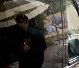 Thomas · 14/05/2026 · 3029 x 3786 Cette photographie montre un homme sous un parapluie transparent, sujet principal partiellement visible à travers la vitre d’un véhicule. La composition est centrée sur ce reflet, avec une ambiance floue et légèrement déformée.Le cadrage est serré, capturant principalement l’intérieur du véhicule et son occupant. La lumière est tamisée, probablement due à la pluie ou à un temps couvert. Les couleurs dominantes sont des tons gris et verts, renforçant une ambiance humide et neutre. Le style est documentaire et spontané, évoquant une scène de vie quotidienne. L’ambiance est mélancolique et intimiste.