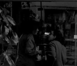 Thomas · 14/05/2026 · 3073 x 4096 Cette photographie en noir et blanc capture une scène intimiste dans un cadre restreint, probablement un restaurant ou un bar.Le **sujet principal** semble être deux personnes assises, l’une prenant une photo avec son téléphone. La **composition** est serrée, centrée sur les visages et les mains, avec un léger flou d’arrière-plan.Le **cadrage** est rapproché, créant une ambiance chaleureuse et confidentielle. La **lumière** est douce et tamisée, avec des contrastes marqués, accentuant les ombres et les détails.Les **couleurs dominantes** sont les nuances de gris, renforçant l’aspect dramatique et intemporel. Le **style** est réaliste et documentaire, tandis que l’**ambiance** est à la fois intime et légèrement mélancolique.