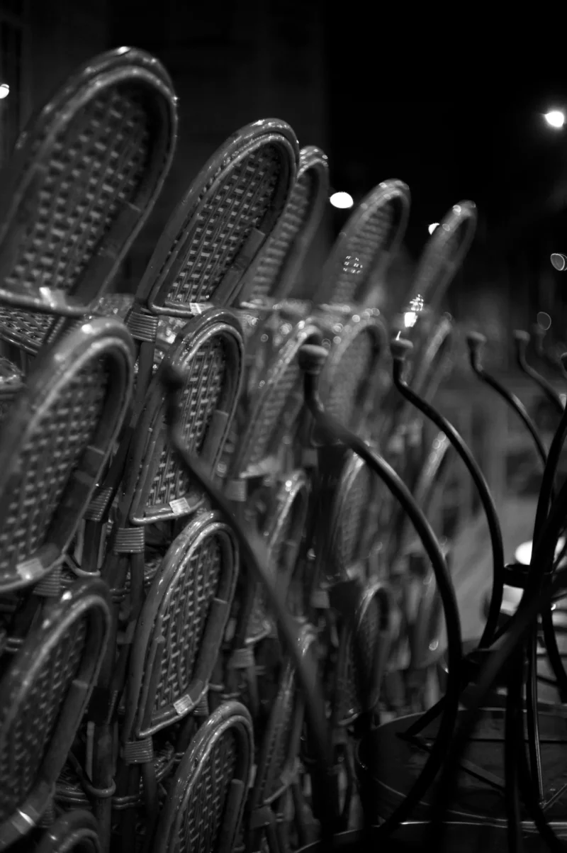 Thomas · 15/05/2026 · 1362 x 2048 Cette photographie en noir et blanc montre des **paires de chaussures de ski** alignées sur une paroi métallique. Le **sujet principal** est ces chaussures, disposées de manière ordonnée et répétitive.La **composition** est symétrique et géométrique, avec un **cadrage serré** qui met en valeur les détails. La **lumière** est tamisée, créant des contrastes marqués et des ombres profondes. Les **couleurs dominantes** sont les nuances de gris, renforçant l’aspect industriel et minimaliste.Le **style** est épuré et presque abstrait, évoquant une **ambiance froide et structurée**, presque clinique.
