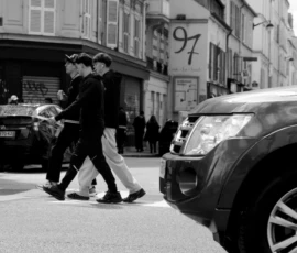 Thomas · 16/05/2026 · 3080 x 2048 Cette photographie en noir et blanc capture deux hommes marchant côte à côte sur un trottoir urbain. Le sujet principal est leur silhouette, en mouvement, au premier plan.La composition met en valeur une rue étroite avec des voitures stationnées et des bâtiments en arrière-plan. Le cadrage est serré, centré sur les deux personnages, avec une profondeur de champ qui floute légèrement les éléments lointains.La lumière est naturelle, probablement en journée, créant des contrastes marqués. Les tons dominants sont les gris et noirs, typiques du noir et blanc, renforçant une ambiance urbaine et intemporelle. Le style est documentaire et réaliste.