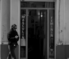Thomas · 16/05/2026 · 1362 x 2048 Cette photographie en noir et blanc met en scène un homme à vélo passant devant une boutique de coiffure nommée "Bigoudi Coiffure". Le sujet principal est l’homme, cadré en mouvement, avec une composition dynamique.La lumière est naturelle, probablement en fin de journée, créant des ombres marquées. Le cadrage inclut une partie du trottoir et de la façade, avec des éléments comme des enseignes et des affiches. L’ambiance est urbaine et quotidienne, renforcée par le style documentaire et le contraste des tons clairs et sombres. L’absence de couleurs accentue les textures et les jeux d’ombres.