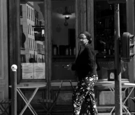 Thomas · 16/05/2026 · 1362 x 2048 Cette photographie en noir et blanc met en scène une personne comme sujet principal, vêtue d’un manteau et de bottes à carreaux, marchant près d’une vitrine. La composition est simple et épurée, avec un cadrage serré sur le sujet et un arrière-plan urbain flou.La lumière semble naturelle, douce, et crée des contrastes marqués. Les ombres et les jeux de lumière accentuent les détails du visage et des vêtements. L’ambiance est à la fois intime et mélancolique, renforcée par le monochrome. Le style rappelle le photojournalisme classique, avec une touche documentaire.