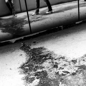 Laurence · 03/05/2026 · 900 x 900 Cette photographie en noir et blanc capture une scène urbaine hivernale. Le sujet principal est une flaque d’eau mélangée à de la neige fondante sur un trottoir, avec des traces de pas et de saleté.La composition met en valeur une ligne diagonale formée par la flaque, menant vers un véhicule partiellement visible. Le cadrage est serré, centré sur le sol, avec une légère perspective ascendante. La lumière semble naturelle, mais contrastée, accentuant les textures et ombres.Les tons dominants sont les gris et noirs, renforçant une ambiance froide et réaliste, typique d’un style documentaire ou street photography.