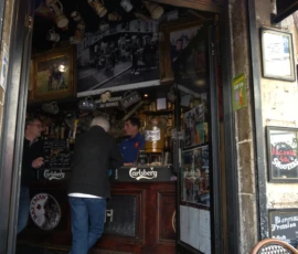 Bao · 6024 x 4016 Cette photographie montre l'intérieur d'un bar traditionnel. Le sujet principal est un comptoir de bar avec des bouteilles et des verres, derrière lequel deux personnes sont visibles.La composition est serrée, centrée sur l'entrée du bar. Le cadrage est serré, mettant en valeur les détails du comptoir et les clients. La lumière est tamisée, créant une ambiance chaleureuse et intimiste. Les couleurs dominantes sont les tons bruns, noirs et dorés, renforçant l'atmosphère rétro et conviviale. Le style évoque un bar classique et authentique, avec une ambiance chaleureuse et accueillante.