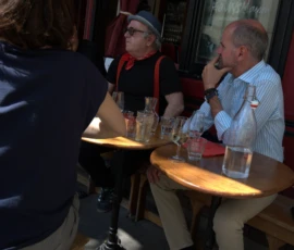 Bao · 4828 x 4016 Cette photographie montre trois hommes assis autour d'une table dans un café. Le sujet principal est leur interaction sociale.La composition est serrée, centrée sur la table et les visages. Le cadrage est en plan moyen, capturant les détails des expressions et des objets.La lumière est douce et naturelle, probablement artificielle, créant une ambiance chaleureuse. Les couleurs dominantes sont les tons chauds : beige, rouge et bleu clair.Le style est documentaire et spontané, évoquant une ambiance conviviale et détendue.