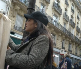 Bao · 4931 x 4016 Cette photographie montre une femme comme sujet principal, vêtue d’un manteau texturé et d’un chapeau, le visage partiellement caché. La composition met en valeur son profil, avec un cadrage serré sur son visage et ses épaules.L’arrière-plan, flou, révèle une rue urbaine avec des immeubles aux balcons en fer forgé. La lumière est naturelle, légèrement tamisée, créant des contrastes doux. Les couleurs dominantes sont les tons neutres (beige, gris) avec des touches de vert et de brun.Le style est documentaire et spontané, évoquant une ambiance urbaine et intime, presque mélancolique.
