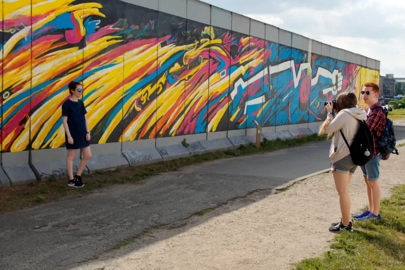 Cédric · 25/05/2017 · 2048 x 1365 Cette photographie montre deux personnes devant un mur tagué. Le sujet principal est le graffiti coloré et dynamique, aux traits épais et aux couleurs vives (jaune, rouge, bleu, noir).La composition place les deux individus en premier plan, l’un photographiant le mur, l’autre observant. Le cadrage est serré sur le mur et les personnes, avec une légère profondeur de champ. La lumière est naturelle, éclatante, créant des contrastes nets. L’ambiance est urbaine, artistique et vivante, reflétant la culture street art.