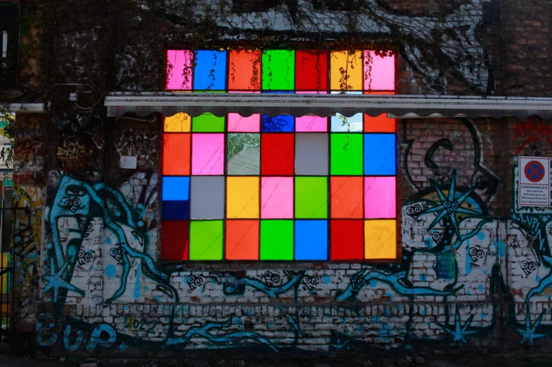 Cédric · 30/04/2026 · 2048 x 1365 Cette photographie met en scène un **mur tagué** avec une **grille colorée** composée de post-it, disposée en forme de damier. Le **sujet principal** est cette mosaïque de couleurs vives, contrastant avec le graffiti sombre et dégradé en arrière-plan.La **composition** est symétrique et géométrique, avec un **cadrage serré** centré sur les post-it. L’**ambiance** est à la fois **urbaine et artistique**, mêlant désordre et ordre. Les **couleurs dominantes** sont les tons vifs des post-it (rouge, bleu, vert, jaune) opposés aux teintes sombres et grises du graffiti. La **lumière** semble naturelle, mettant en valeur les contrastes. Le style est **urbain et créatif**.