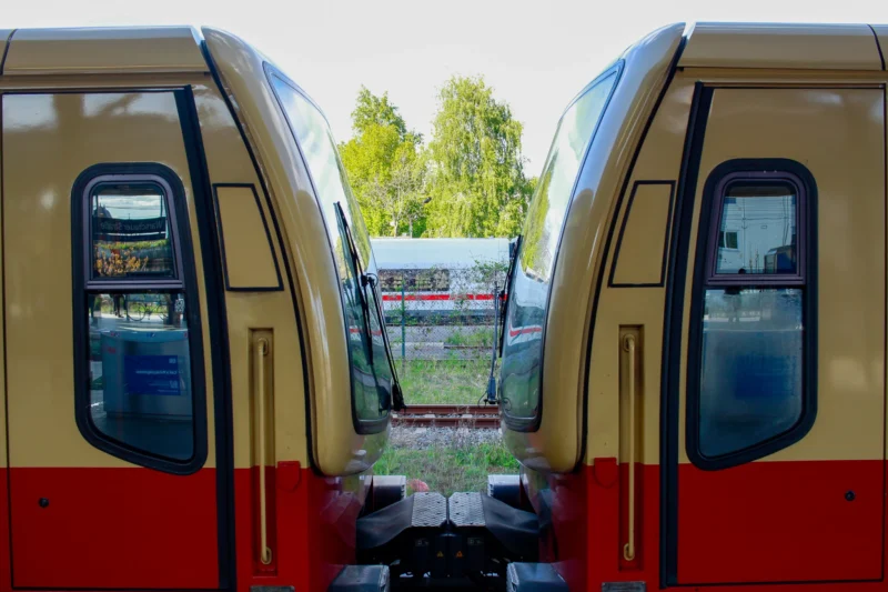 Cédric · 30/04/2026 · 2048 x 1365 Cette photographie montre deux trains en miroir, formant un effet de symétrie. Le sujet principal est l’espace entre les deux véhicules, révélant un paysage extérieur flou.La composition repose sur un cadrage serré et une perspective centrale, créant une illusion de profondeur. La lumière est naturelle, douce, et semble provenir d’une journée ensoleillée mais non aveuglante. Les couleurs dominantes sont le rouge vif des trains et les tons neutres (beige, gris) des structures.Le style est épuré et géométrique, évoquant une ambiance moderne et industrielle, tout en apportant une touche poétique grâce à la symétrie.