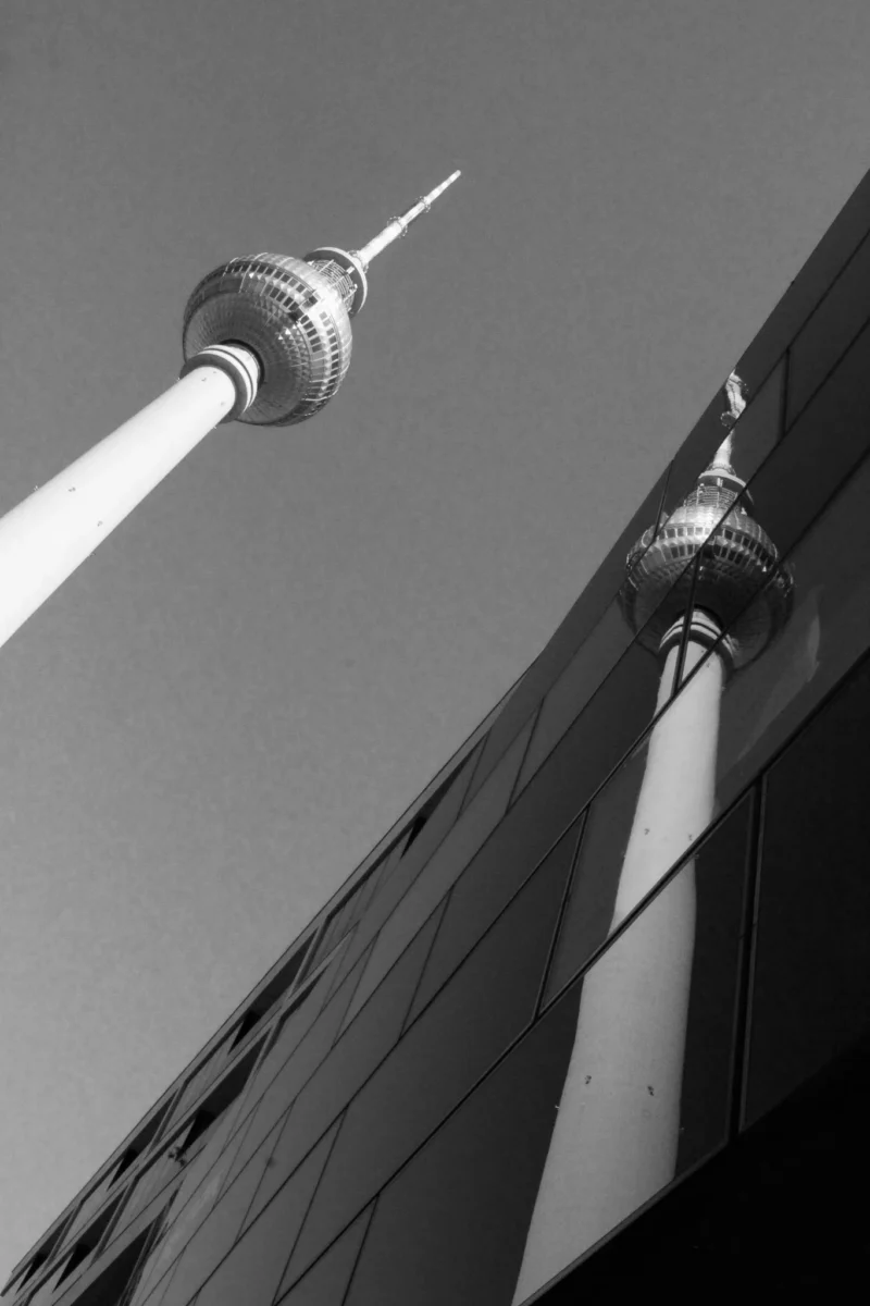 Cédric · 01/05/2026 · 1365 x 2048 Cette photographie met en scène la tour Fernsehturm de Berlin, sujet principal identifiable par sa sphère et son antenne. La composition joue sur les lignes verticales et horizontales, avec un cadrage serré qui accentue la hauteur et la modernité de l'édifice. La lumière, douce et uniforme, crée des contrastes nets entre ombres et lumières, typiques d’un cliché en noir et blanc. Les tons gris dominent, renforçant une ambiance à la fois minimaliste et dramatique. Le style est épuré, soulignant l’architecture et la géométrie de la structure. L’ambiance est à la fois futuriste et intemporelle.