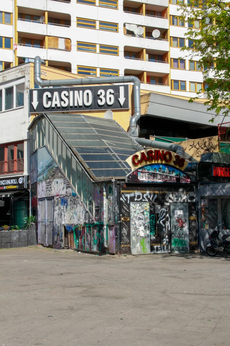 Cédric · 02/05/2026 · 1365 x 2048 Cette photographie montre un ancien **Casino 36**, aujourd’hui transformé en lieu couvert et tagué. Le **sujet principal** est ce bâtiment aux allures abandonnées, avec des enseignes délavées et des graffitis omniprésents.La **composition** est serrée, avec un **cadrage en plan moyen**, mettant en valeur les détails architecturaux et les tags. La **lumière** naturelle, probablement en journée, éclaire les tons sans être trop vive. Les **couleurs dominantes** sont grises, noires (graffitis) et quelques touches de vert et rouge.L’ambiance est **urbaine, délabrée et nostalgique**, reflétant un style **street art** et une atmosphère de déclin.