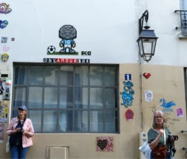 Bao · 5565 x 3147 Cette photographie montre un groupe de personnes devant une façade décorée de stickers et graffitis. Le sujet principal semble être un lieu coloré et artistique, probablement un bar ou un café nommé "Intergalactico".La composition met en avant les éléments décoratifs et les personnes en bas à gauche. Le cadrage est serré sur la façade et les individus. La lumière est naturelle et semble provenir du jour, éclairant uniformément la scène. Les couleurs dominantes sont vives et variées, avec des tons pastel et des touches de bleu, rose et vert.L’ambiance est décontractée et créative, évoquant un lieu convivial et artistique.