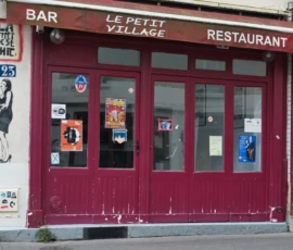 Fahad · 14/05/2026 · 3000 x 2000 Cette photographie montre la façade d’un petit restaurant-bar nommé **« Le Petit Village »**. Le sujet principal est l’entrée rouge avec ses portes vitrées et ses enseignes.La composition est symétrique, centrée sur les portes. Le cadrage est serré, mettant en valeur les détails comme les affiches et graffitis. La lumière semble naturelle, douce et légèrement tamisée.Les couleurs dominantes sont le rouge vif des portes et le blanc des enseignes, avec des touches de noir et de gris sur les affiches. Le style est urbain et authentique, évoquant une ambiance chaleureuse et conviviale, typique d’un établissement local.