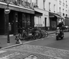 Fahad · 14/05/2026 · 3000 x 2000 Cette photographie en noir et blanc capture une scène urbaine calme. Le sujet principal est un groupe de vélos et motos garés le long d’un trottoir, avec une moto en premier plan. La composition est symétrique et ordonnée, avec des bâtiments en arrière-plan et une rue pavée en bas.Le cadrage est serré, mettant en valeur les détails des véhicules et l’architecture. La lumière est douce, sans ombres marquées, créant une ambiance sobre et intemporelle. Les tons de gris dominent, accentuant l’aspect rétro et urbain. Le style est documentaire, évoquant une atmosphère paisible et quotidienne dans une ville européenne.