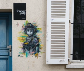 Fahad · 14/05/2026 · 2000 x 3000 Cette photographie montre un mural street art représentant un soldat stylisé, avec des couleurs vives et des traits expressifs. Le sujet principal est ce graffiti, encadré par une fenêtre blanche entrouverte et une enseigne "foggar" à gauche.La composition est équilibrée, avec un cadrage serré sur le mural et la fenêtre. La lumière naturelle éclaire uniformément la scène, mettant en valeur les détails. Les couleurs dominantes sont les tons bleus, verts et jaunes du graffiti, contrastant avec le gris-beige du mur.Le style est urbain et artistique, évoquant une ambiance à la fois moderne et rebelle.