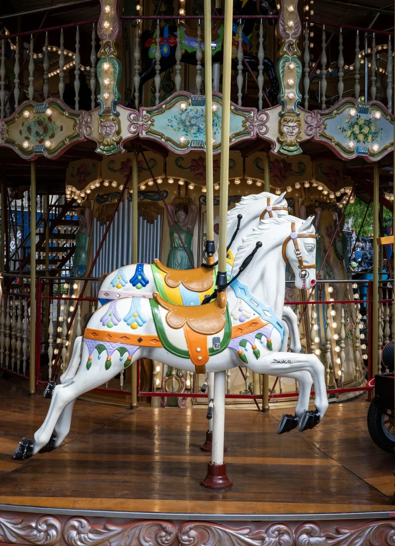 Nathalie C H · 08/05/2026 · 1283 x 1773 Cette photographie met en scène un **cheval de manège** en bois peint, sujet principal. La composition est centrée sur l’animal, avec un cadrage serré qui isole partiellement le fond décoratif.La lumière est douce, mettant en valeur les détails du cheval. Les **couleurs dominantes** sont les tons blancs, ors et bleus pastel, typiques des manèges anciens. Le style évoque une **ambiance rétro et nostalgique**, rappelant les carnavals et fêtes foraines d’autrefois. L’éclairage chaud et les ornements dorés renforcent le charme vintage.