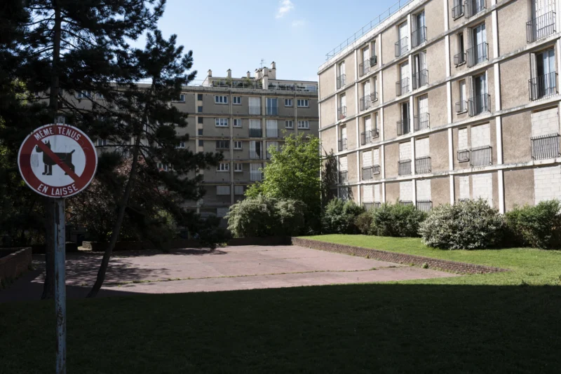 Jean-Philippe · 14/04/2026 · 7616 x 5088 Cette photographie montre un immeuble résidentiel moderne en arrière-plan. Le sujet principal est un panneau "Chiens dangereux interdits". La composition est simple, avec un cadrage centré sur le panneau et une allée menant vers l'immeuble. La lumière est naturelle et claire, suggérant un jour ensoleillé. Les couleurs dominantes sont les tons verts (végétation), gris (bâtiment) et rouge (panneau). Le style est réaliste et documentaire, capturant un environnement urbain calme. L'ambiance est sereine, presque banale, reflétant un quartier résidentiel ordinaire.