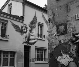 Agnès · 14/05/2026 · 4160 x 6240 Cette photographie en noir et blanc met en scène une façade urbaine ornée d’une sculpture d’ange aux ailes déployées, fixée à un bâtiment. Le cadrage inclut aussi un mur adjacent couvert de graffitis et de tags, créant un contraste entre l’élégance classique et l’art urbain.La composition joue sur les lignes verticales et les textures, tandis que la lumière douce, probablement naturelle, accentue les ombres et les détails. Les couleurs dominantes, bien que monochromes, varient des gris clairs aux noirs profonds, renforçant l’ambiance mélancolique et poétique. Le style mêle réalisme et street art, évoquant une atmosphère à la fois nostalgique et moderne.